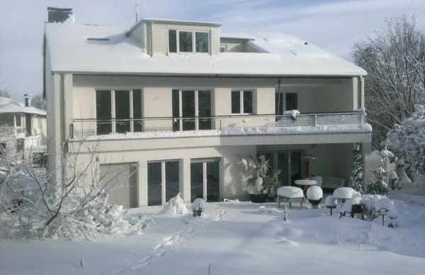 Verschneites saniertes 60er-Jahre-KfW-Haus mit Balkon und Glasfassade.