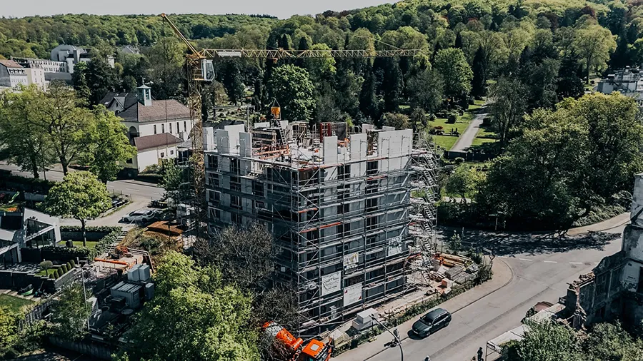 Baustelle am Christbusch mit Kran, Rohbau und Gerüst in grüner Wohnumgebung.