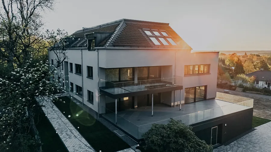 Modernes Mehrfamilienhaus Marper Wohnen mit Balkon, Terrasse und Garten bei Sonnenuntergang.