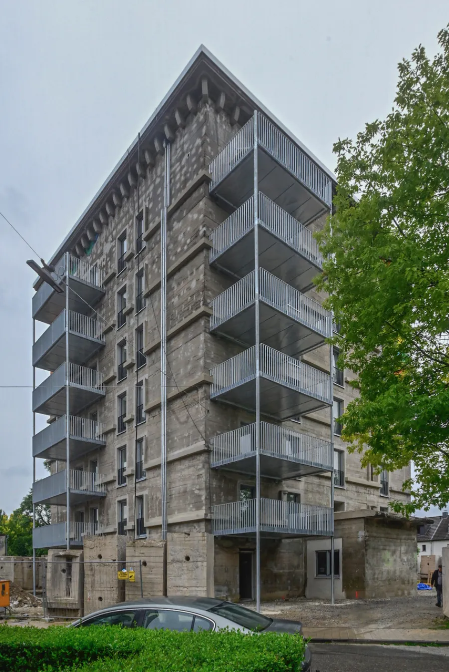 Sanierter Betonbunker mit Metallbalkonen und rauer Fassade in urbaner Umgebung.