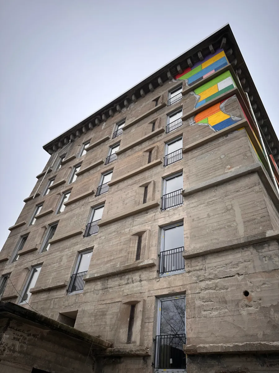 Hohe Bunkerfassade aus Beton mit buntem Wandbild und Fensterreihen.