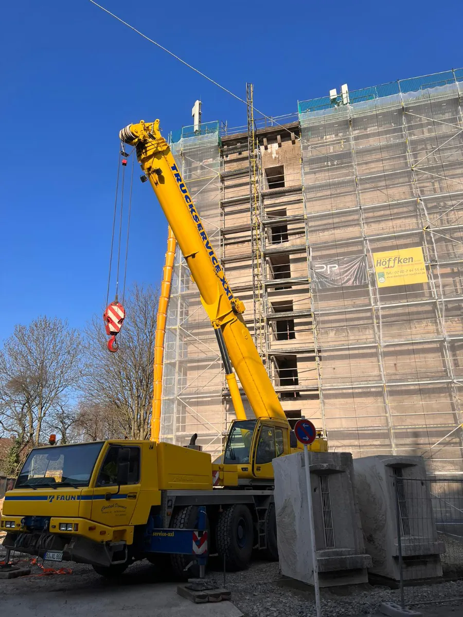 Gelber Kran auf Baustelle vor eingerüstetem Bunker bei Außenarbeiten.