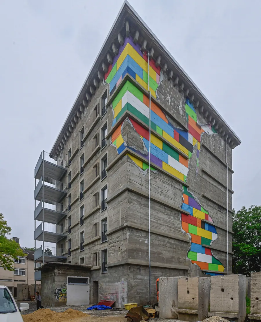 Grauer Betonbunker mit farbenfrohem Street-Art-Mural und Baustelle im urbanen Umfeld.