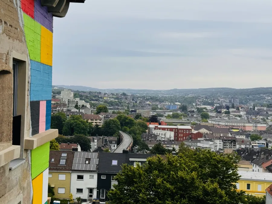 Bunte Bunkerfassade mit Panoramablick über Stadt, Dächer und grüne Hügel.