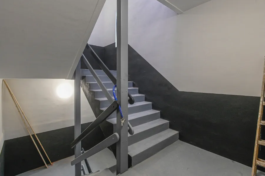 Beton-Treppenhaus im Bunker mit Geländer, Wandlicht und Wartungsleiter.