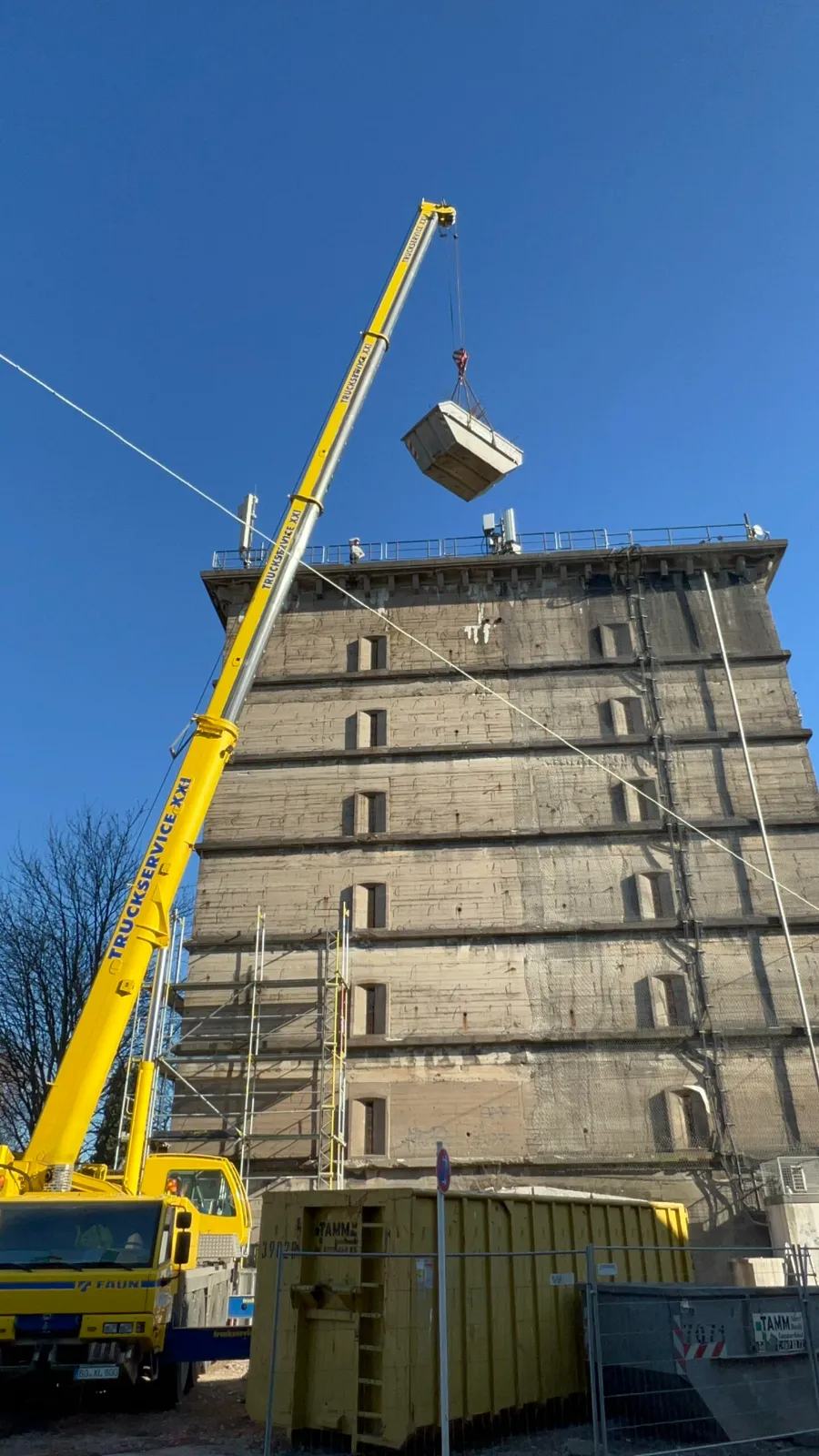 Gelber Kran hebt Container auf Bunkerbaustelle am Hochhaus.