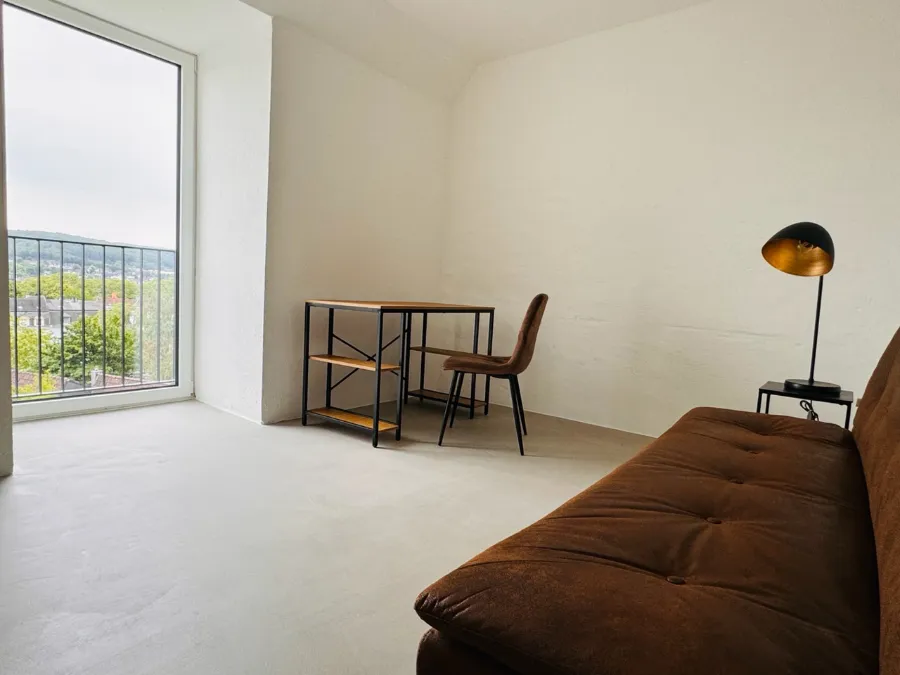 Helles minimalistisches Bunker-Wohnzimmer mit Sofa, Schreibtisch und großem Fenster.