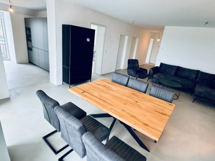 Modernes Bunker-Wohnzimmer mit Essbereich, Eichenholztisch, grauem Sofa und Industriedesign.