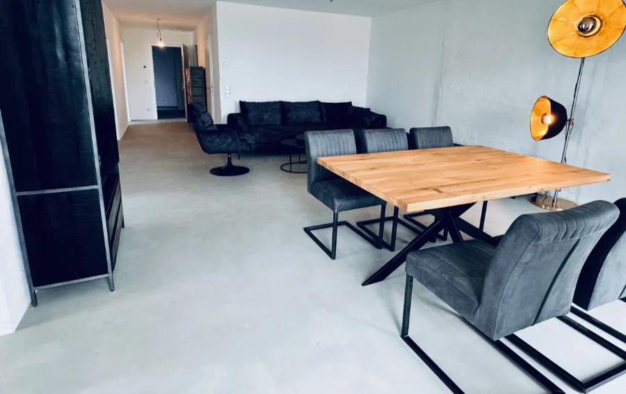 Modernes Industrial Wohnzimmer mit Esstisch, Betonboden und grauem Sofa.