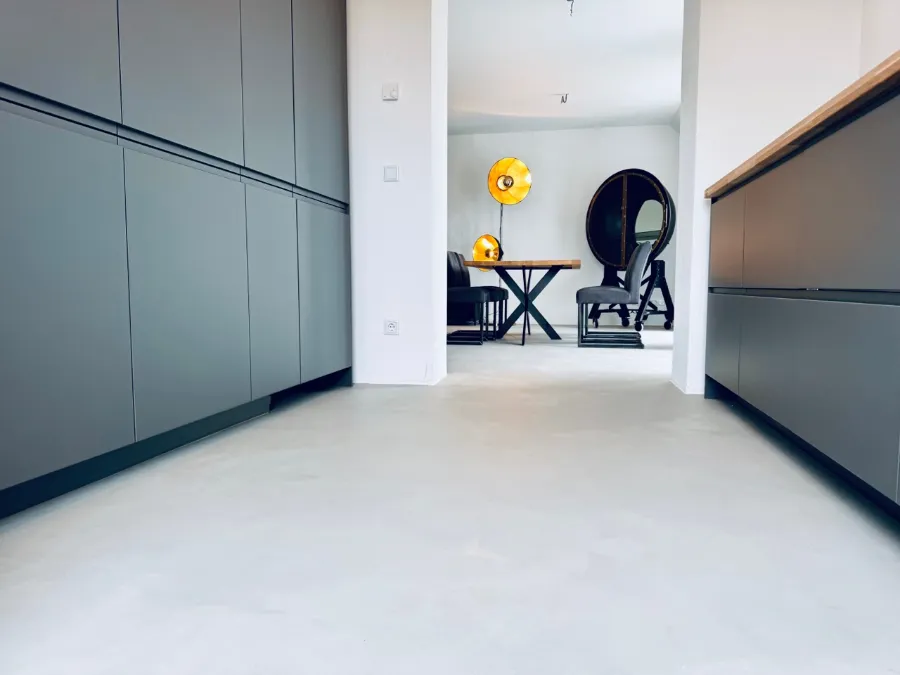 Moderner Betonboden in minimalistischer Küche mit Essbereich, Holztisch und goldenen Stehlampen.