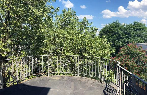 Sonniger Balkon am Christbusch mit Metallgeländer, grünen Bäumen und blauem Himmel.