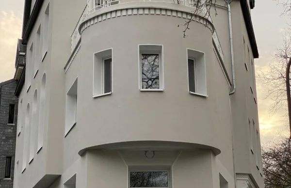 Helle Stadtvilla mit runder Eckfassade, schmalen Fenstern und modernem Eingang.