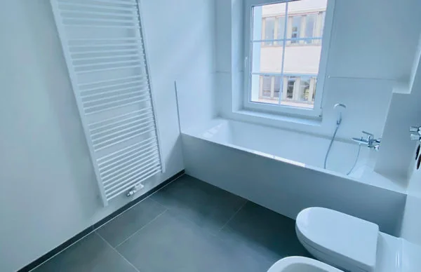 Modernes Badezimmer mit Badewanne, Fenster, WC, Bidet und Handtuchheizkörper.
