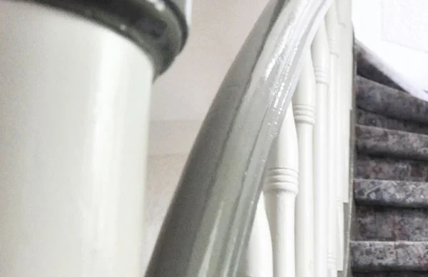 Treppengeländer mit weißen Balustern und gemustertem Teppichläufer im Altbau.