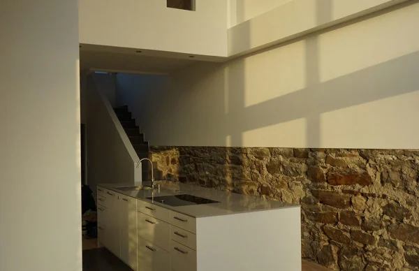 Moderne weiße Kücheninsel im Backsteinhaus mit Natursteinwand und warmem Sonnenlicht.