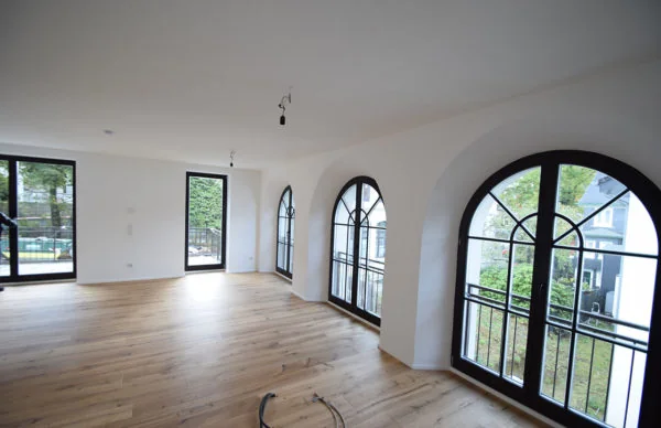Heller renovierter Wohnraum mit Holzboden, weißen Wänden und großen Bogenfenstern.