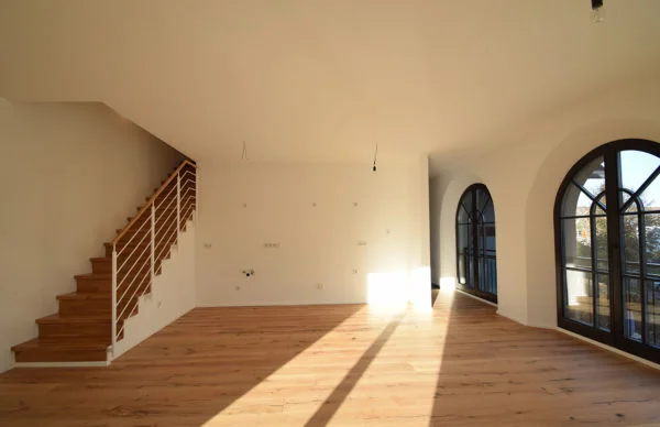 Heller Wohnraum mit Rundbogenfenstern, Holzfußboden und moderner Treppe.