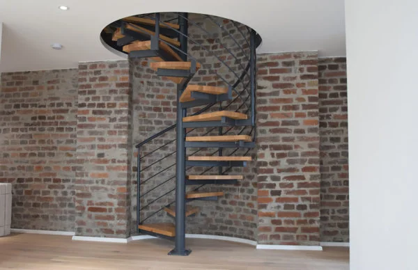 Moderne Wendeltreppe aus Holz und Stahl vor rustikaler Backsteinwand.