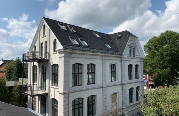 Historisches Schulgebäude Glocke mit Mansarddach, Rundbogenfenstern und sanierter Stuckfassade.