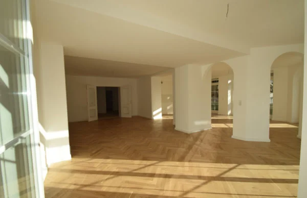 Lichtdurchfluteter Wohnraum in Villa mit Fischgrätparkett, Rundbögen und großen Fenstern.