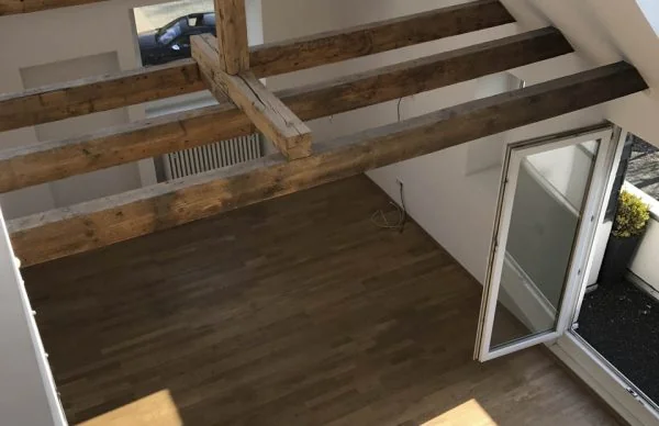 Loft-Innenraum mit Holzbalken, Parkettboden und offener Balkontür in ehemaliger Bürovilla.