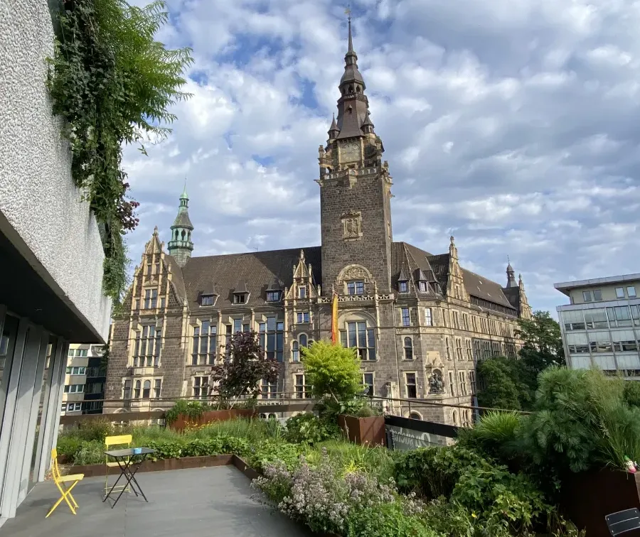 Gewächshaus-Terrasse mit Pflanzen und Blick auf historisches Rathaus am Neumarkt.