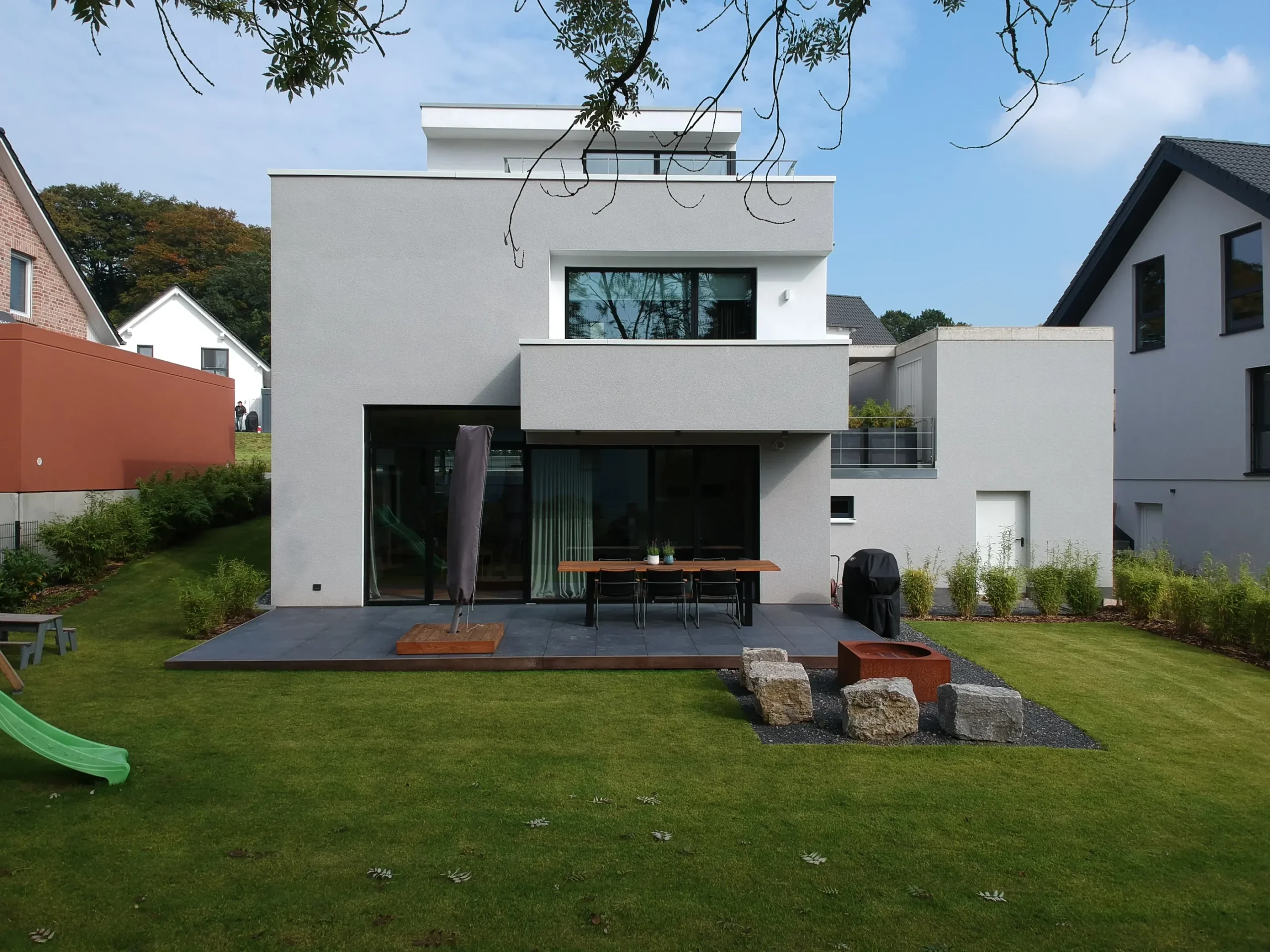 Modernes Einfamilienhaus mit Garten, Terrasse, Glasfront und minimalistischer Architektur.
