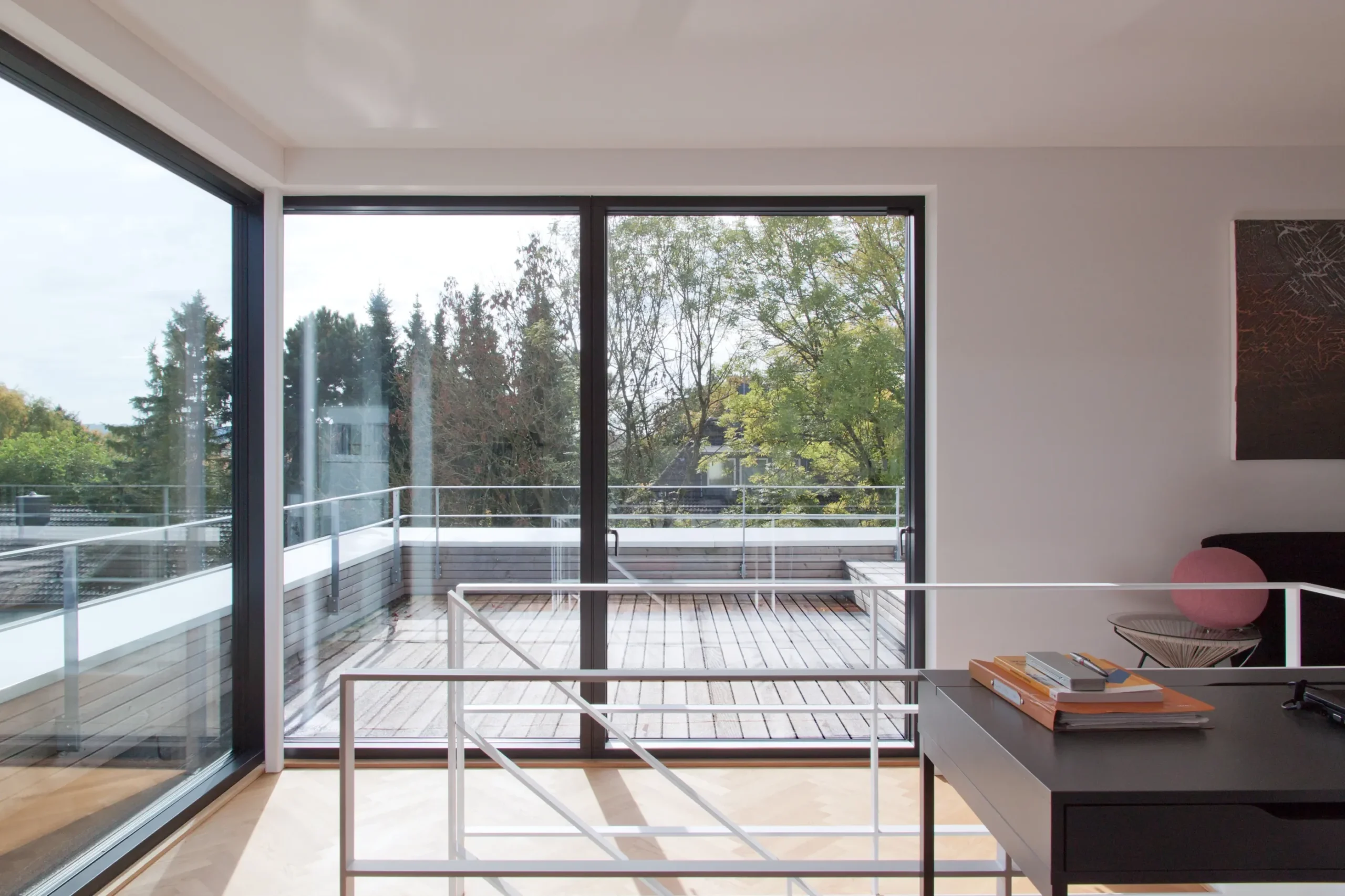 Moderner Wohnraum mit bodentiefen Glas-Schiebetüren, Holzterrasse und Blick ins Grüne.