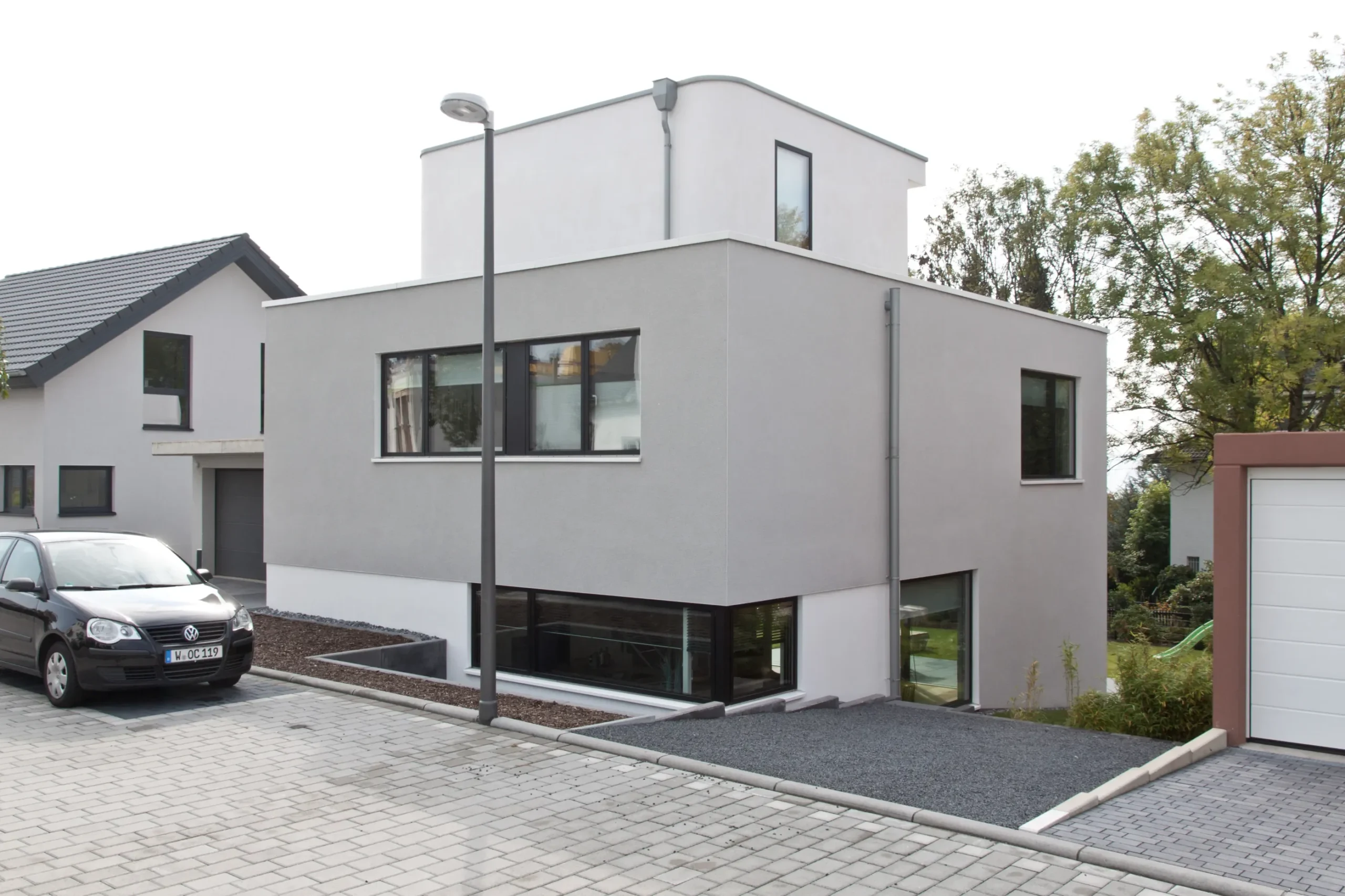 Modernes Einfamilienhaus mit grauer Fassade, großen Fenstern und gepflasterter Einfahrt.