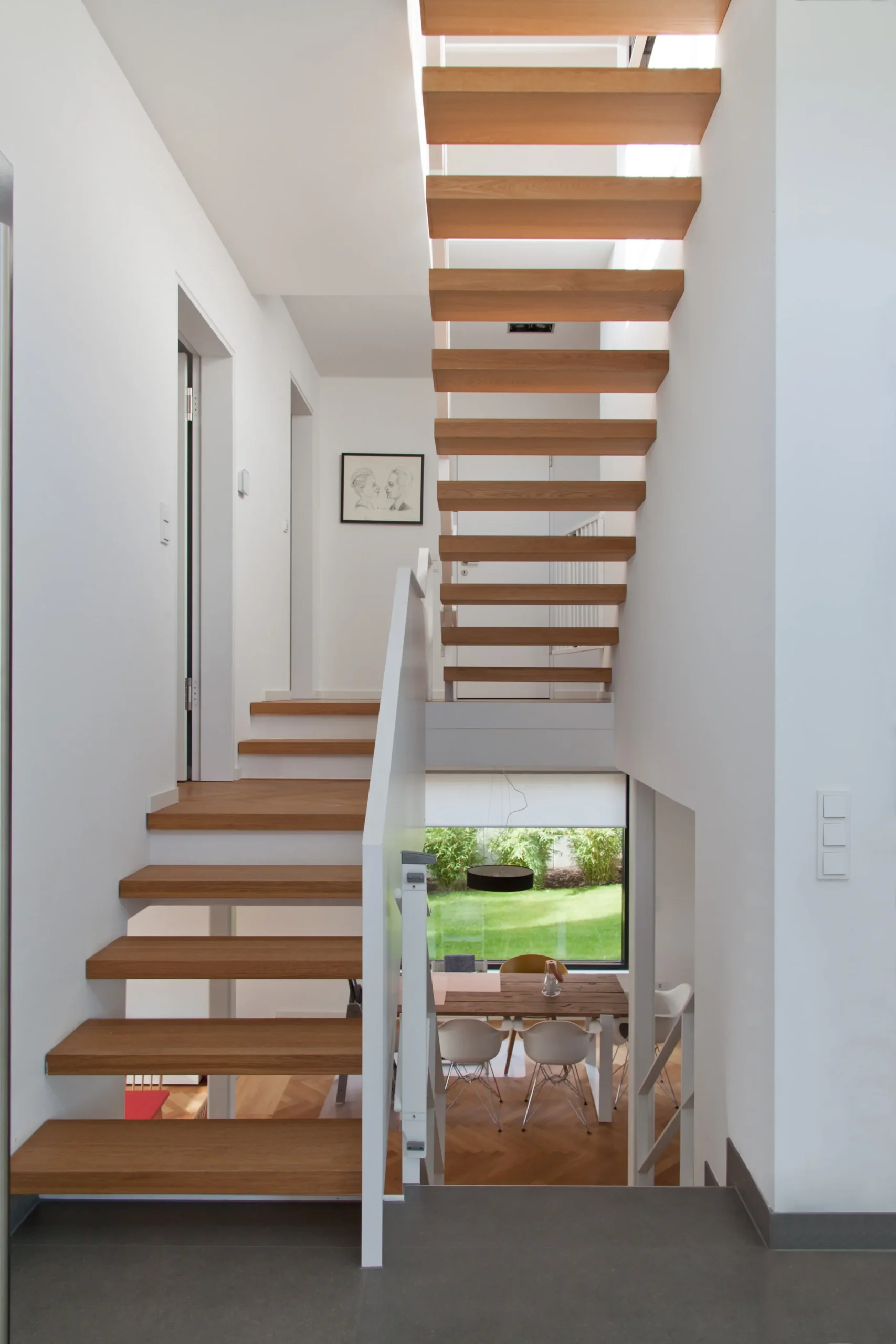 Moderne Holztreppe mit offenen Stufen in hellem Wohnhaus und Blick zum Garten.