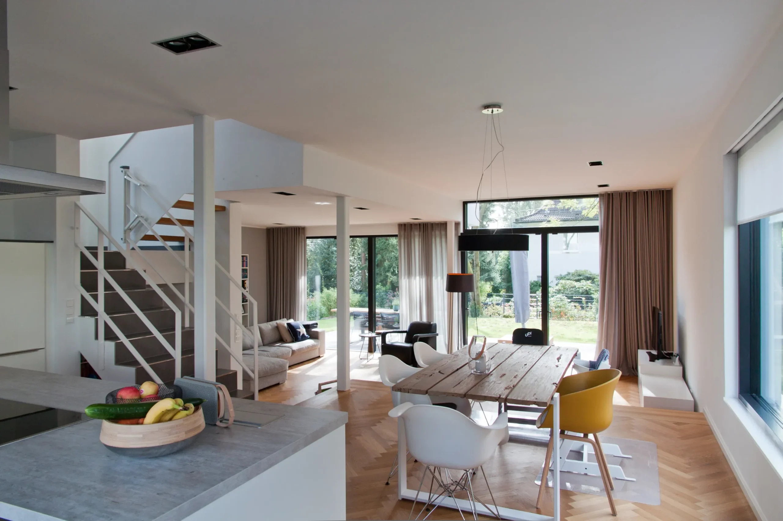 Modernes offenes Wohnkonzept mit Küche, Essbereich, Holztisch und Gartenblick.