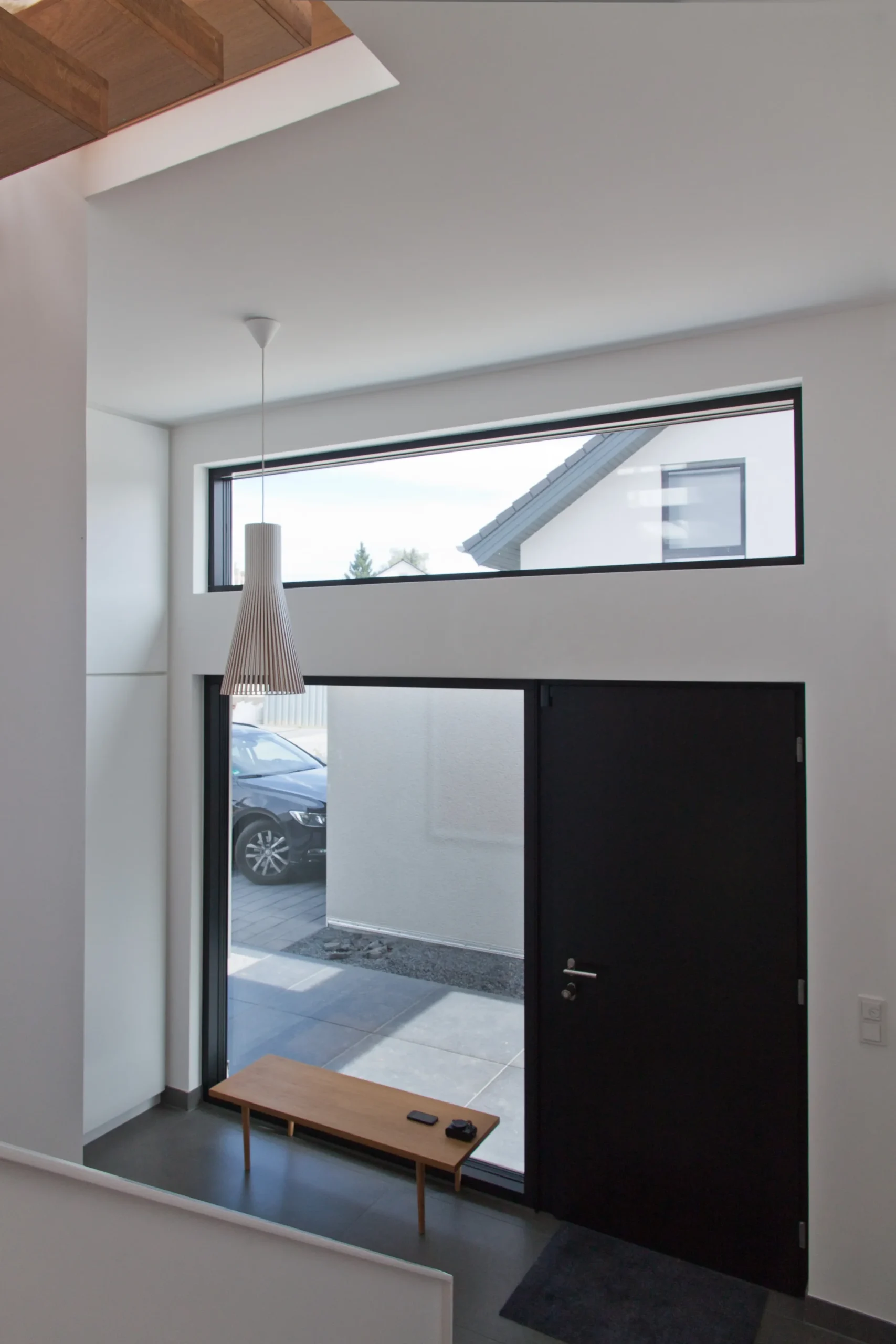 Moderner Eingangsbereich mit Glasfront, schwarzer Haustür, Sitzbank und Tageslicht.