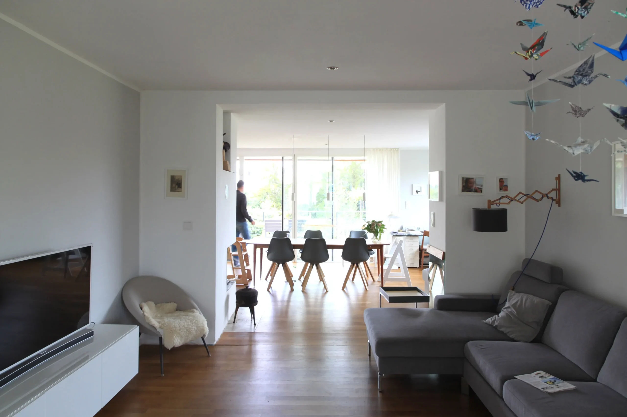 Modernes Wohnzimmer mit offenem Essbereich, Holzboden, grauem Sofa und großen Glasschiebetüren.