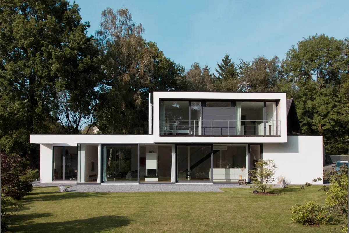 Modernes weißes Architektenhaus mit Glasfassade, Balkon und gepflegtem Garten.