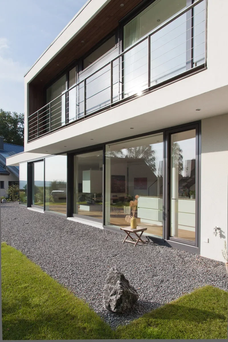 Modernes zweistöckiges Architektenhaus mit Glasfassade, Balkon und minimalistischer Gartengestaltung.