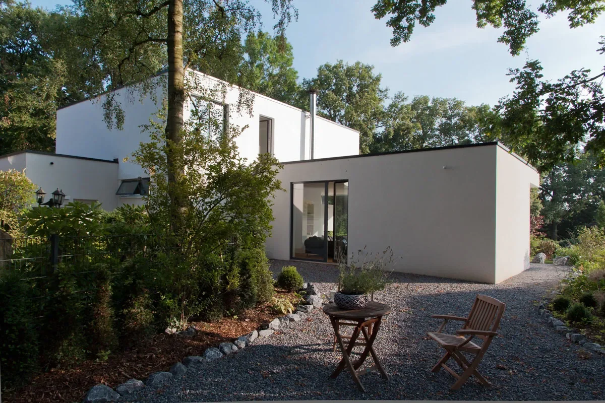 Modernes weißes Haus mit Garten, Kieshof, Terrasse und großen Glasfronten.