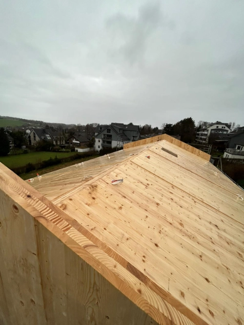 Neues Holzhaus im Bau mit frisch verlegtem Holzdach im Wohngebiet.