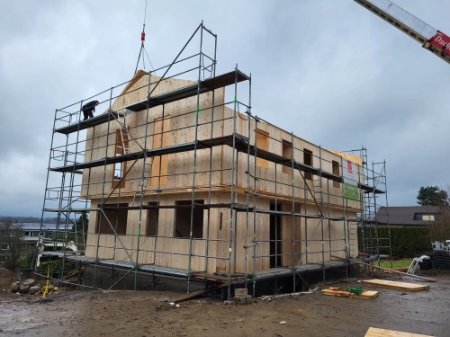 Holzhaus im Bau mit Gerüst und Kran auf Baustelle.