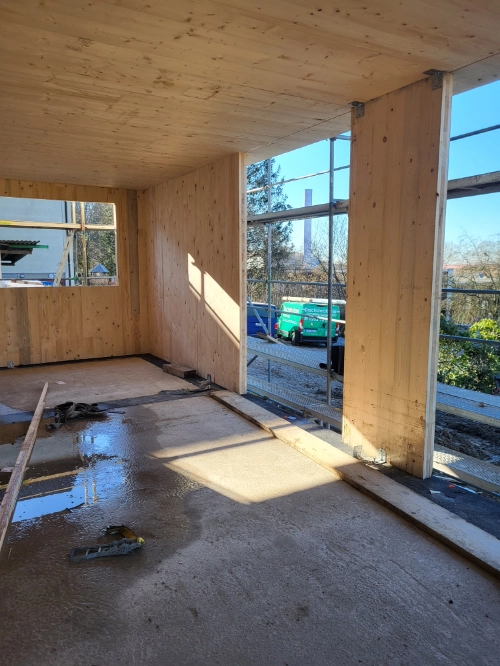 Innenausbau eines Holzhauses mit Massivholz-Wänden, Baustelle und großen Fensteröffnungen.