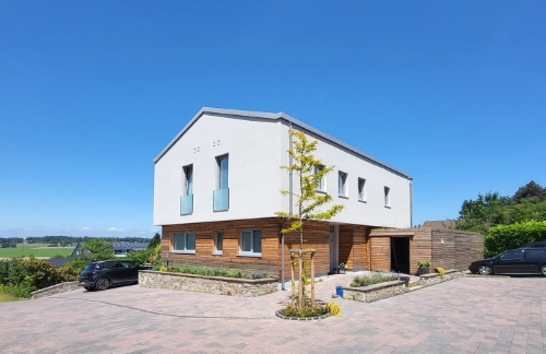 Modernes Holzhaus mit weißer Fassade, gepflasterter Einfahrt und ländlicher Landschaft.