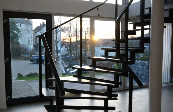 Moderne Loftwohnung mit schwarzer Wendeltreppe, bodentiefen Fenstern und Sonnenuntergang.