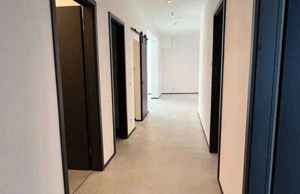 Moderner Loft-Flur in Ronsdorf mit weißen Wänden, dunklen Türrahmen und Betonboden.