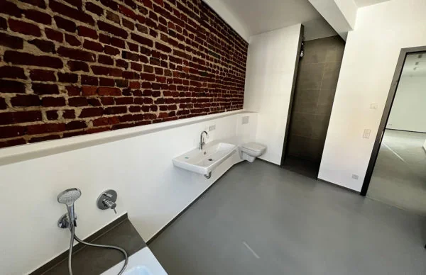 Modernes Loft-Badezimmer mit Backsteinwand, grauem Boden und minimalistischen Sanitäranlagen.