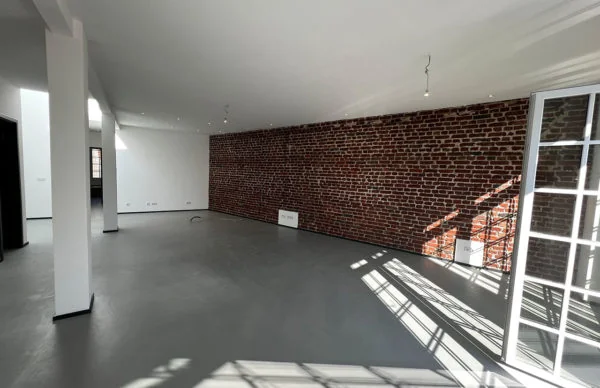 Modernes Loft in Ronsdorf mit Backsteinwand, grauem Boden und hellem Tageslicht.