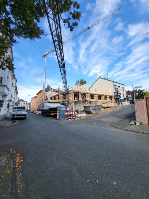 Massivholz-Mehrfamilienhaus im Bau mit Kran und Gerüst an urbaner Straßenecke.
