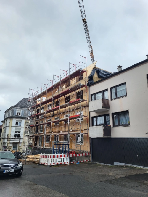Massivholz Mehrfamilienhaus im Bau mit Gerüst und Kran.