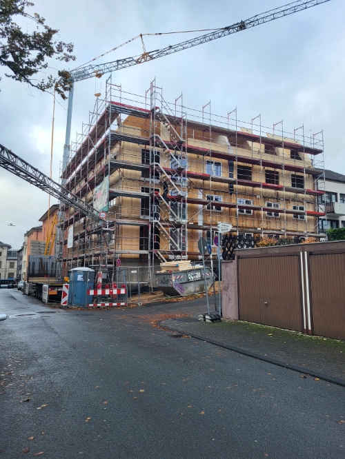 Massivholz-Mehrfamilienhaus im Bau mit Gerüst und Kran auf urbaner Baustelle.