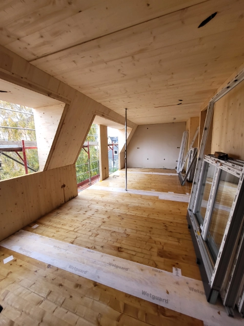 Massivholz-Mehrfamilienhaus im Innenausbau mit Holzverkleidung, Baustelle und großen Fensteröffnungen.
