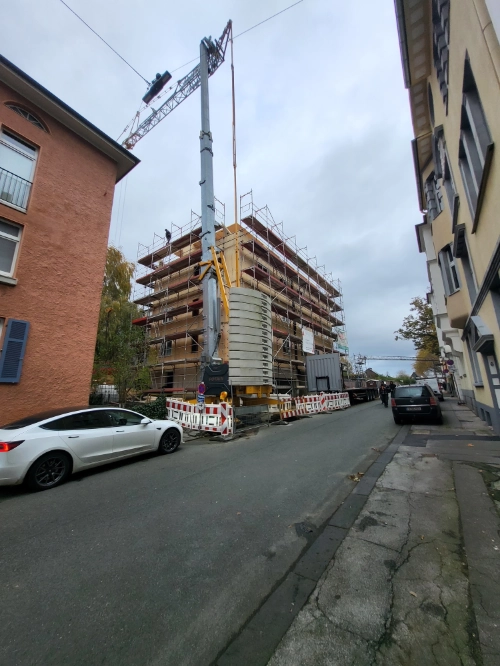 Massivholz-Mehrfamilienhaus im Bau mit Kran und Gerüst in urbaner Straße.