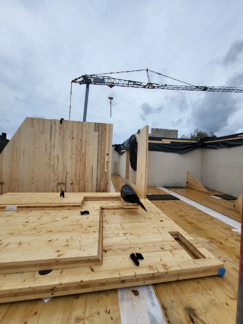Massivholz-Mehrfamilienhaus im Bau mit Holzpanelen, Kran und Rohbau auf Baustelle.